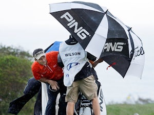 Mark Wilson and his caddy hide behind their umbrella during the windy weather in Hawaii on January 7, 2013