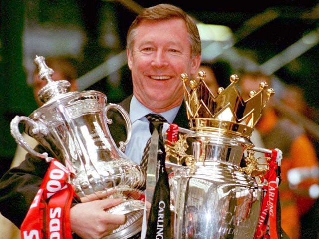 Manchester United manager Alex Ferguson proudly displays the FA Cup and Premier League trophies