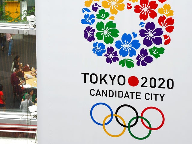 People walk under the bid emblem of the Tokyo 2020 Olympic and Paralympic Games hoisted in downtown Tokyo on September 7, 2013