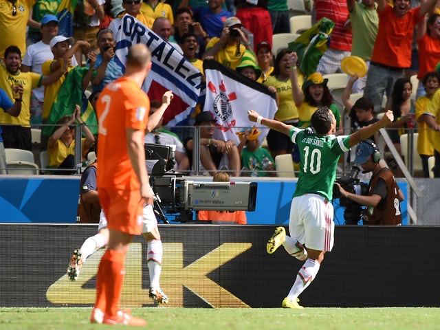 Mexico's forward Giovani Dos Santos is watched by Netherlands' defender Ron Vlaar as he celebrates with teammates after scoring during a Round of 16 football match between Netherlands and Mexico at Castelao Stadium in Fortaleza during the 2014 FIFA World 