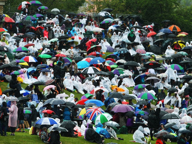 Fans sitting on Murray mound shelter under umbrellas as rain delays the start of play on day six of the Wimbledon Lawn Tennis Championships on June 28, 2014