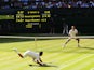 Novak Djokovic of Serbia dives to make a return as Roger Federer of Switzerland stands at the net during the Gentlemen's Singles Final match at Wimbledon on July 6, 2014