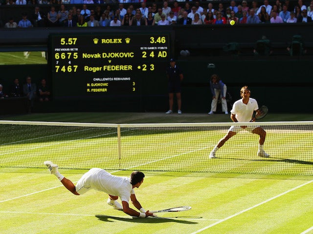 Novak Djokovic of Serbia dives to make a return as Roger Federer of Switzerland stands at the net during the Gentlemen's Singles Final match at Wimbledon on July 6, 2014