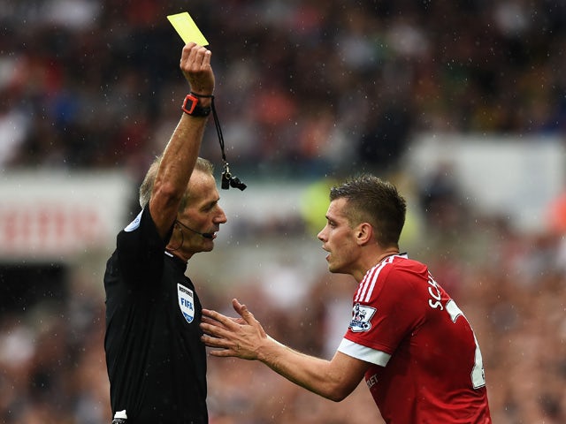 Referee Martin Atkinson shows the yellow card to Morgan Schneiderlin of Manchester United during the Barclays Premier League match between Swansea City and Manchester United at Liberty Stadium on August 30, 2015