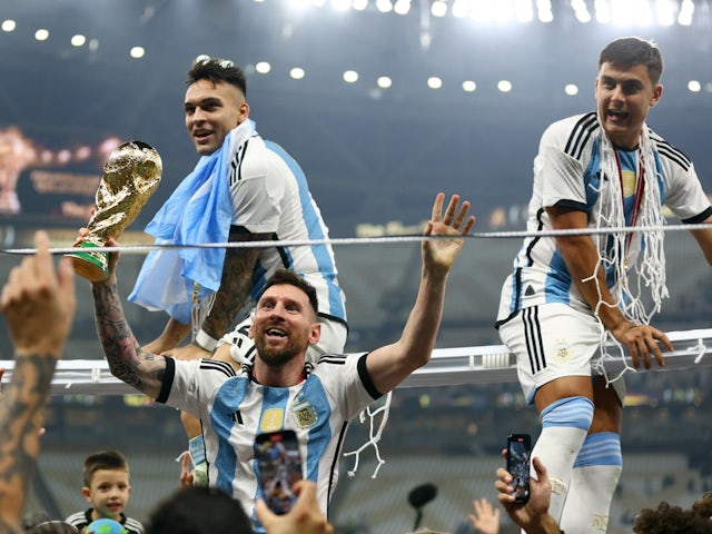 Argentina's Lionel Messi celebrates winning the World Cup with the trophy along with Lautaro Martinez and Paulo Dybala on December 18, 2022